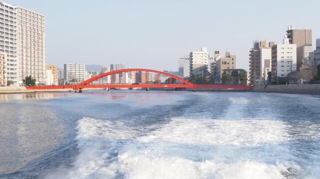 Slow motion landscape of whitewater trailing from ferry passenger boat moving along river canals with the Sumiyoshi Bridge and urban buildings in the background Motoyasu Hiroshima city Japan travel