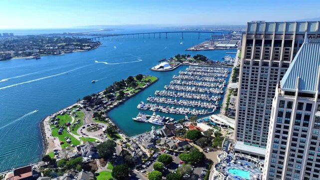 Aerial view of downtown San Diego waterfront with the Manchester Grand Hyatt, Embarcadero Marina Park South, marina boats, the Rady Shell, and Coronado Bridge on a bright clear day.