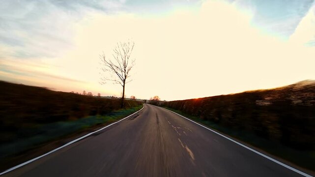 Racing along curved rural road at sunset with motion blur, countryside travel adventure point of view. Empty asphalt lane bending through hedgerows under glowing evening sky, road trip freedom POV