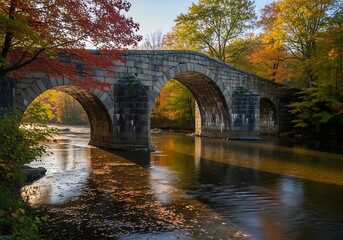 Fototapeta premium Ancient stone bridge amidst autumnal forest and flowing river