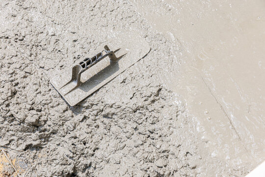 Top view of a plastic trowel tool resting on a freshly smoothed wet concrete floor surface at a construction site.