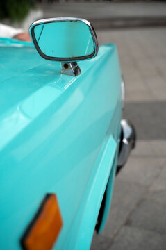 Side view mirror on a vintage convertible in bright turquoise.