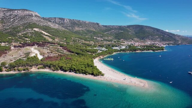 Aerial view of Zlatni Rat's iconic, sandy peninsula kissed by turquoise waters, set against a backdrop of lush green hills, Bol, Dalmatian Coast, Croatia.