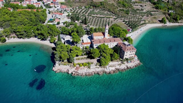 Aerial view of a monastery nestled on a rocky peninsula surrounded by turquoise water and a sandy beach, Bol, Dalmatian Coast, Croatia.