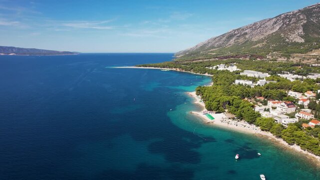 Aerial view of the vibrant turquoise sea meeting the sandy beach near the forested coastline, Zlatni Rat Beach, Bol, Dalmatian Coast, Croatia.