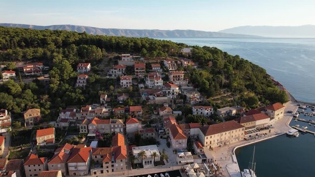 Aerial view of Jelsa town and harbor, where terracotta roofs meet the Adriatic's turquoise waters amidst lush green hills, Jelsa, Split-Dalmatia County, Croatia.