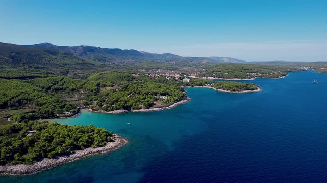 Aerial view of the vivid Jelsa coastline, where the deep blue sea meets verdant green forests under a clear sky, Jelsa, Split-Dalmatia County, Croatia.