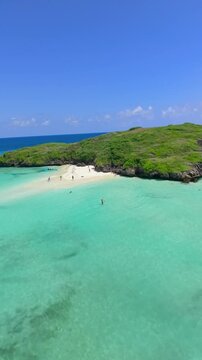 Aerial view of people on a white sand beach surrounded by turquoise water and green rocky islands at Watamu Beach, Kenya.