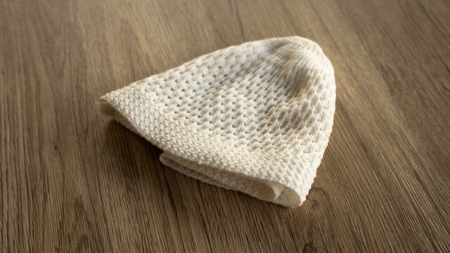 White Knitted Muslim Prayer Cap or Kopiah on Wooden Texture Background