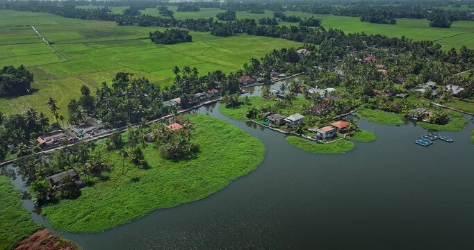 Aerial view of the Alleppey backwaters in Kerala showing traditional boats, narrow canals, palm-lined banks, village houses, and lush green paddy fields, famous tourism destination in South India.