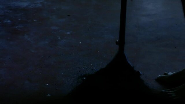 Silhouette of a person sweeping dust with a broom in a dark moody interior at night cinematic