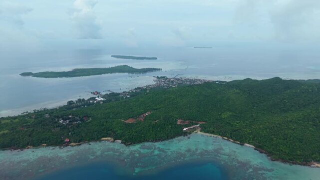Aerial view of Karimunjawa Island revealing lush green vegetation, turquoise waters, and a coastal settlement nestled along the serene shoreline, Karimunjawa, Central Java, Indonesia.
