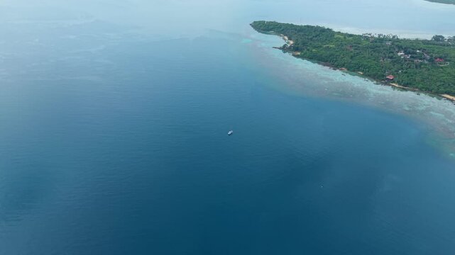 Aerial view of a tropical island showcasing lush green trees and clear waters gently lapping onto the shore, Karimunjawa, Central Java, Indonesia.