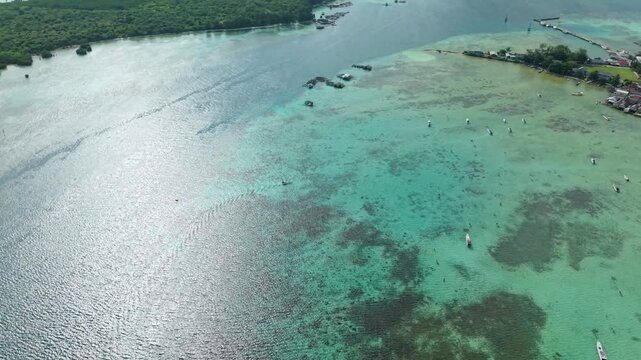Aerial view of boats dotting the turquoise waters near houses, contrasting with the darker sea, showcasing a vibrant coastal scene, Karimunjawa, Central Java, Indonesia.