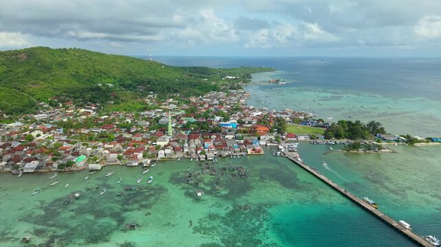 Aerial view of Karimunjawa village showing the vibrant green island meeting the vivid turquoise sea, with boats dotting the landscape, Karimunjawa, Central Java, Indonesia.