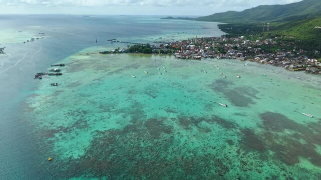 Aerial view of boats scattered across turquoise waters near the coastal houses, a picturesque scene showcasing the blend of human settlement and ocean, Karimunjawa, Central Java, Indonesia.