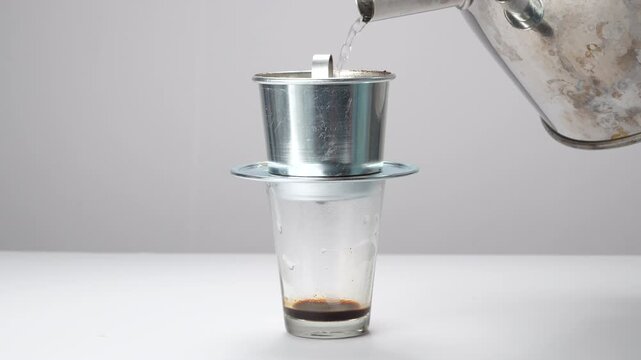 Hand places lid on a traditional Vietnamese phin filter as dark coffee drips into a glass. Commercial footage of authentic Asian brewing.