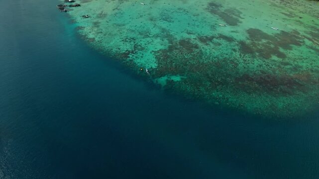Aerial view of clear turquoise waters surrounding vibrant reefs and small boats near the island, creating a stunning contrast with the deep blue sea, Karimunjawa, Central Java, Indonesia.
