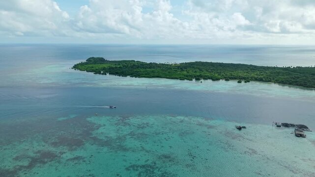 Aerial view of a boat sailing on the turquoise water between islands with lush green vegetation under a cloudy sky, Karimunjawa, Central Java, Indonesia.