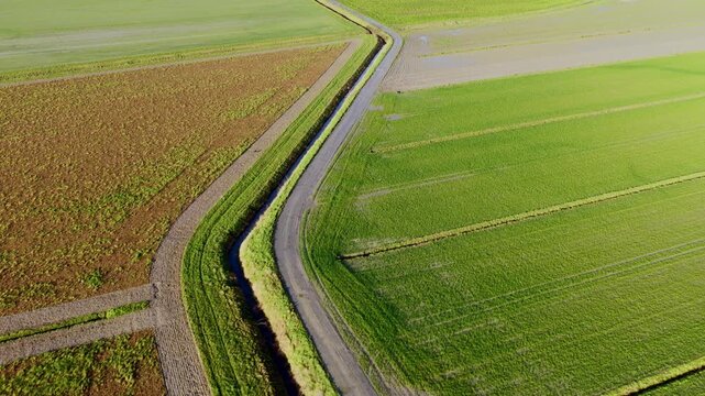 Aerial view of green agricultural fields and a narrow rural road with a drainage ditch in Mont Saint-Michel, Normandy, France.