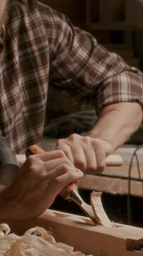 Close up view of woodworker carving timber plank with chisel and mallet at workbench in carpentry workshop. Vertical format video