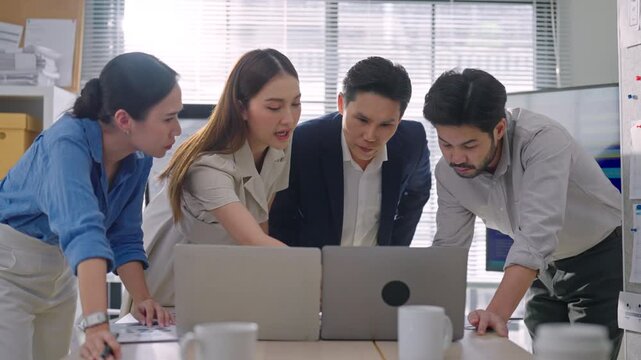 Professional Asian business team meeting discussing project updates and collaborating on laptop during a routine office meeting.