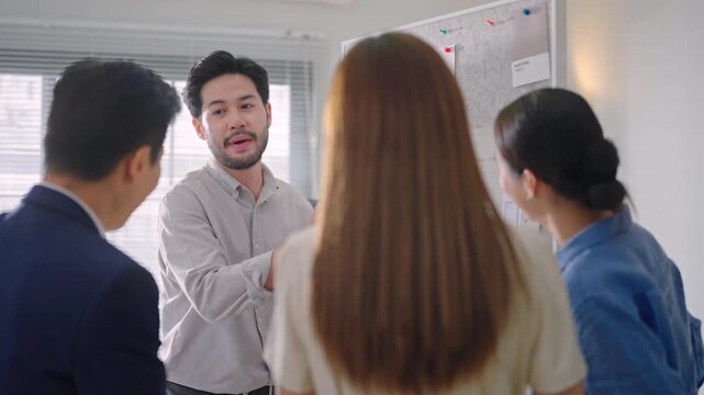 Asian businessman and team discussing application workflow, data analysis, and team tasks pinned on a whiteboard during a strategic meeting.