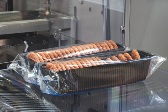 A tray of cookies sits on a packaging conveyor. All the cookies are the same size, lined up in a row, and wrapped in clear plastic film.