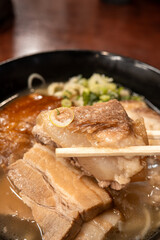Traditional Okinawa Soba noodle soup with pork belly and ribs in a black bowl.