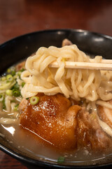 Traditional Okinawa Soba noodle soup with pork belly and ribs in a black bowl.