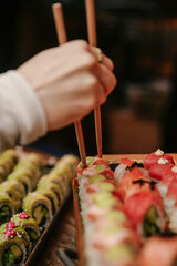 Vertical Close-up of a Guest Using Wooden Chopsticks to Pick Up Fresh Nigiri and Maki Sushi from a Gourmet Catering Display © maorattias