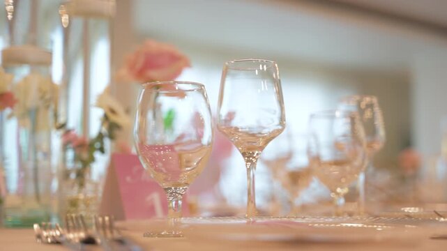 Elegant close-up shot of a refined table setting with crystal wine glasses and delicate floral elements, soft warm lighting, shallow depth of field