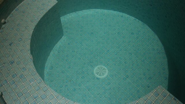 Close-up view of a round tiled plunge pool with blue water and a central drain, creating a calm, private courtyard spa atmosphere
