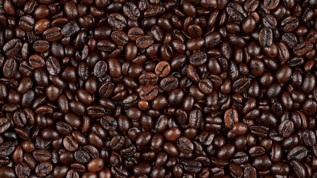Top-down rotating background of dark roasted coffee beans. Premium glossy flat lay texture for cinematic cafe and barista video projects.