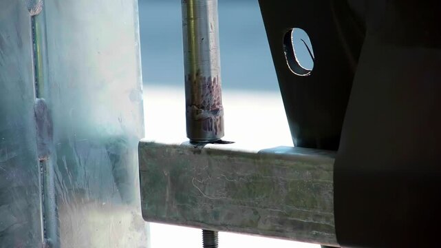 Close up slow motion footage of a metal locking pin and galvanized steel bracket being aligned and secured during industrial assembly or construction installation