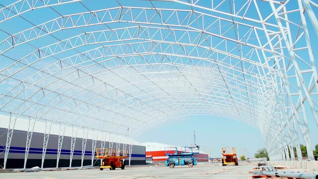 Wide shot of a large steel frame warehouse under construction with elevated work platforms on an industrial building site