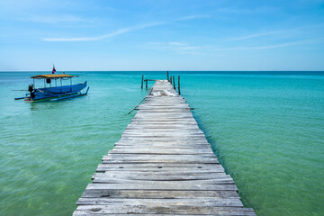 Fototapeta premium Old jetty over turquoise water and traditional cambodian boat on a beach on the island of Koh Rong Sanloem near Sihanoukville, Cambodia