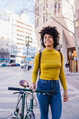Naklejka premium Happy woman with headphones walking bicycle in city