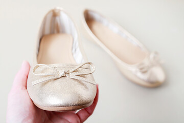 A young woman holds a single golden ballet flat, with the second one visible in the background. The photo is a metaphor for youthful dreams and the desire to set out into the wide world. © agneskantaruk
