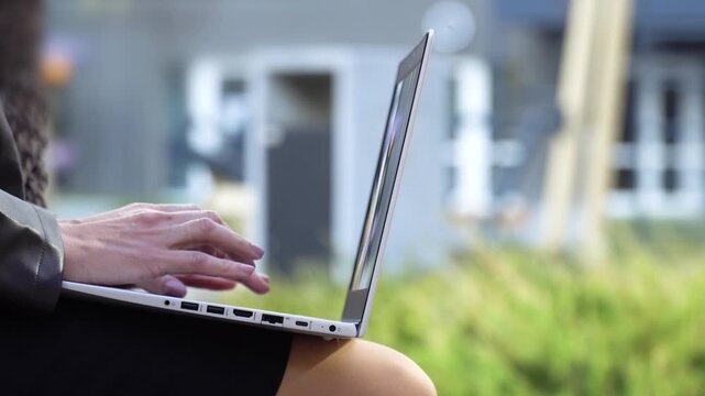 Woman typing on generic laptop outdoors close-up profile, copy space
