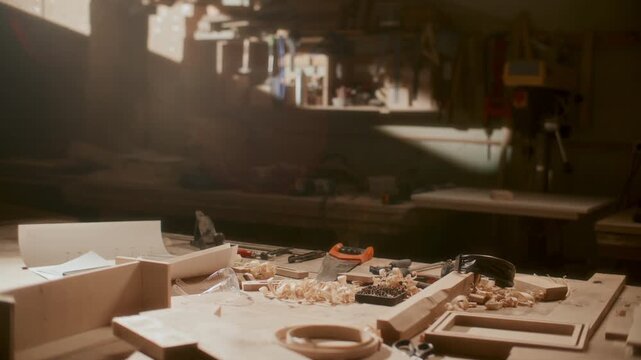 Interior of cozy woodworking workshop with wooden pieces, hand tools, shavings and paper plans scattered across workbench illuminated by warm sunlight
