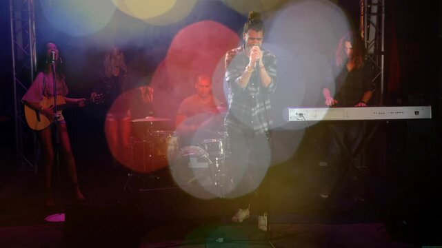 Lead singer gripping mic, singing on dim stage, bokeh orbs shifting, showing band for music show