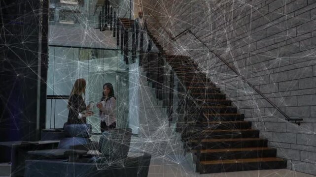 Talking, two women in blazers handing device near window while man descending stairs with folder