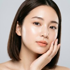 Fototapeta premium Close-up portrait of a beautiful young Asian woman with radiant, glowing skin, gently touching her cheek, embodying natural beauty, health, and effective skincare.