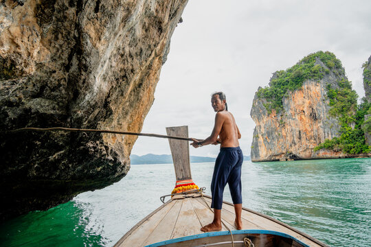 Thai man navigating longtail boat through limestone karst in andaman sea