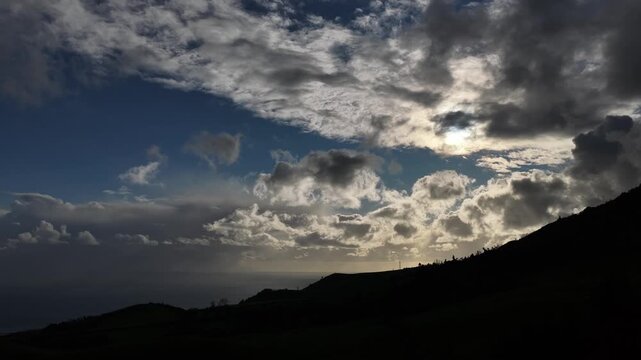 Aerial view of a dark mountain silhouette against a sky filled with dramatic clouds, creating a stark contrast of light and shadow, Ponta Delgada, Portugal.