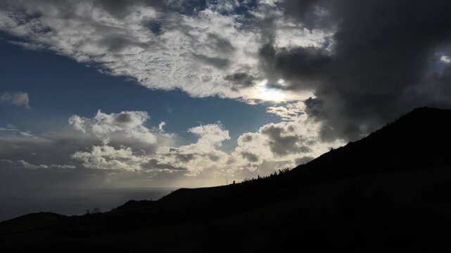 Aerial view of a dark mountain silhouette against a cloudy sky with sunlight breaking through, creating a dramatic contrast, Ponta Delgada, Portugal.
