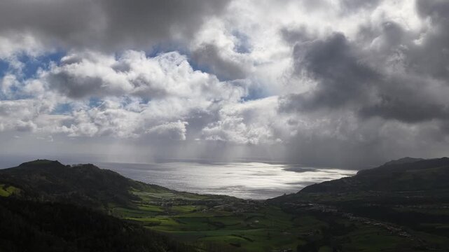 Aerial view of the dramatic coastline where sunbeams pierce through the clouds, illuminating the ocean's surface, Ponta Delgada, Sao Miguel, Portugal.