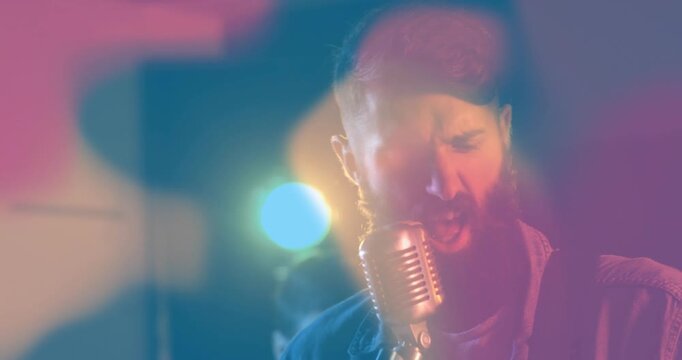 Singing camera-cue vocalist in jacket stepping into retro mic on stage with drums to lead band
