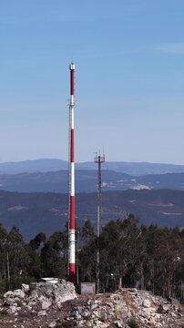 Aerial view of a tall red and white tower rising above the trees, set against a backdrop of distant mountains, Valongo, Portugal.